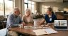 Healthcare professional and two seniors discuss photos at a round table in a lobby setting with a laptop showing patient images on screen